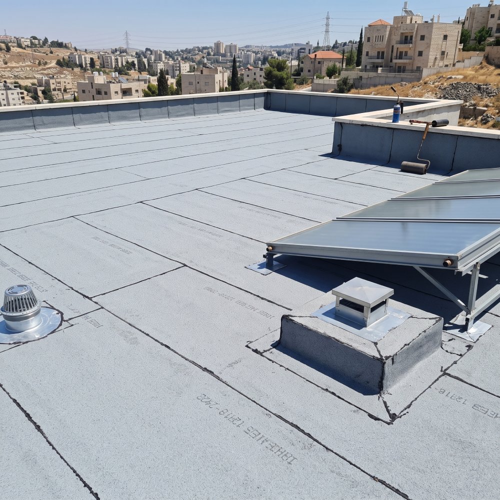 גג שטוח מכוסה יריעות ביטומניות, עם פתח ניקוז ורשת ומעטפת איטום סביב ארובה נמוכה